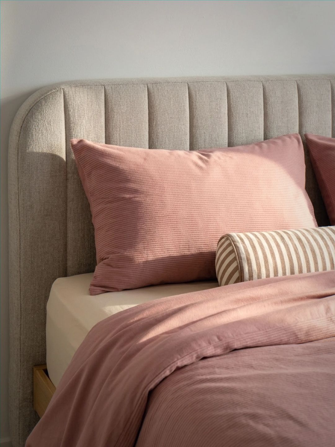 Bed with pink bedding and striped pillow against a neutral headboard