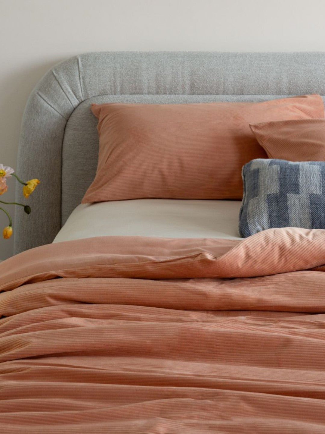 Bed with pink bedding and pillows against a gray headboard