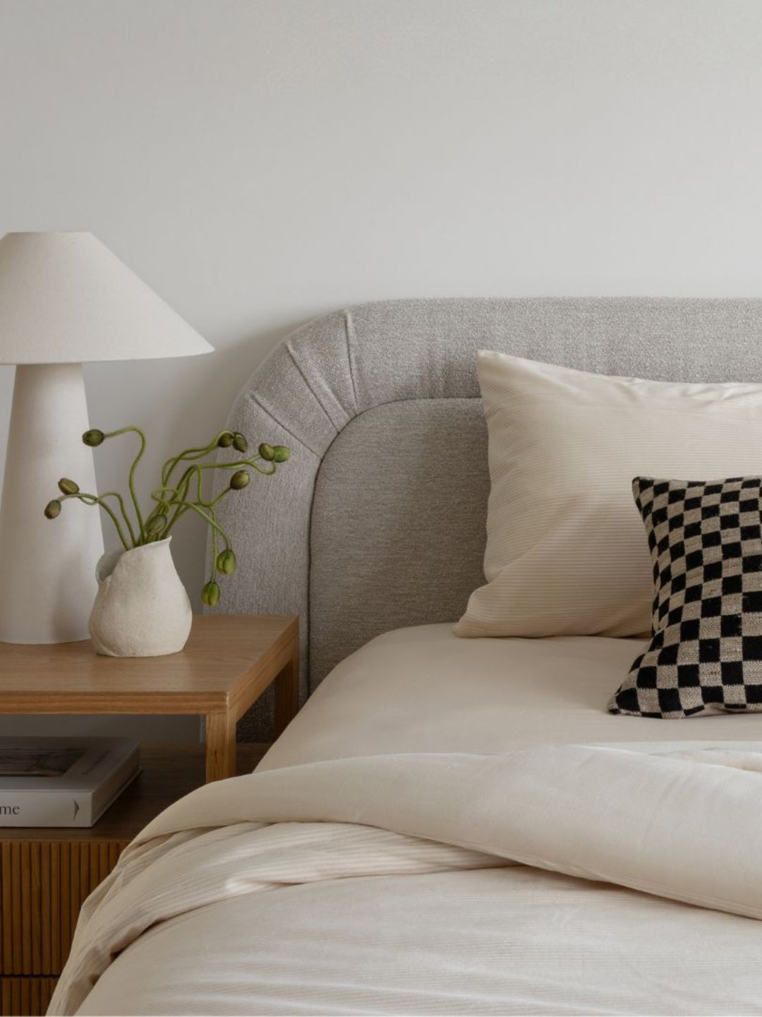 Neatly made bed with pillows and a lamp on a nightstand in a bedroom setting.