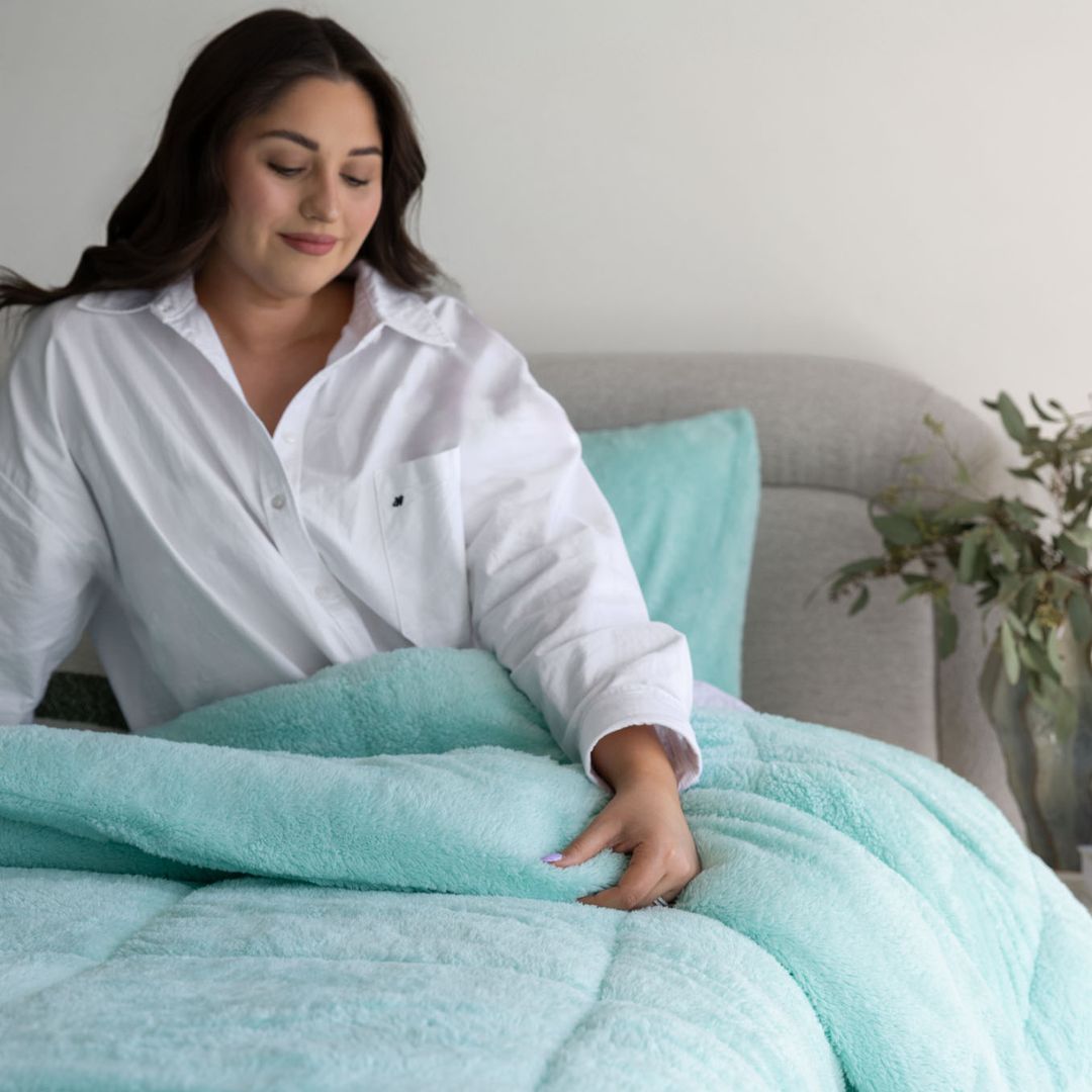 Woman in a white shirt holding a light blue blanket in a cozy room.