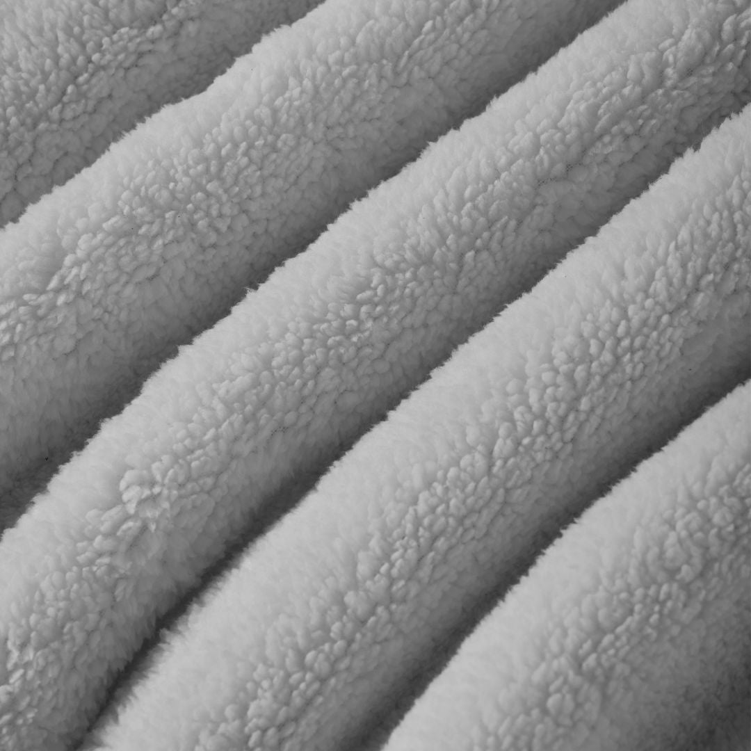 A neatly made bed features the Morgan and Reid Checkered Silver Snuggle Fleece Comforter Set, with matching pillows, a wooden headboard, nightstand with lamp and bottles, a large plant, and a woven pendant light for lasting luxury.