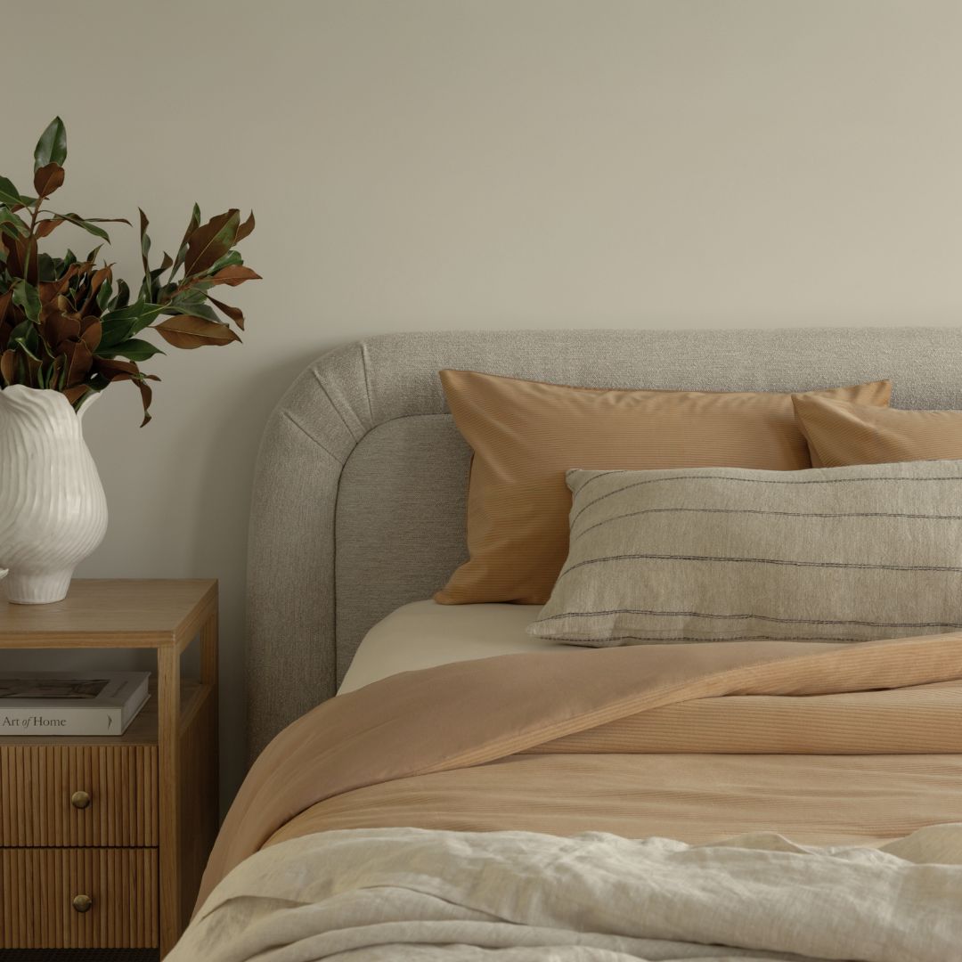 Neatly made bed with beige and brown bedding in a bedroom setting.