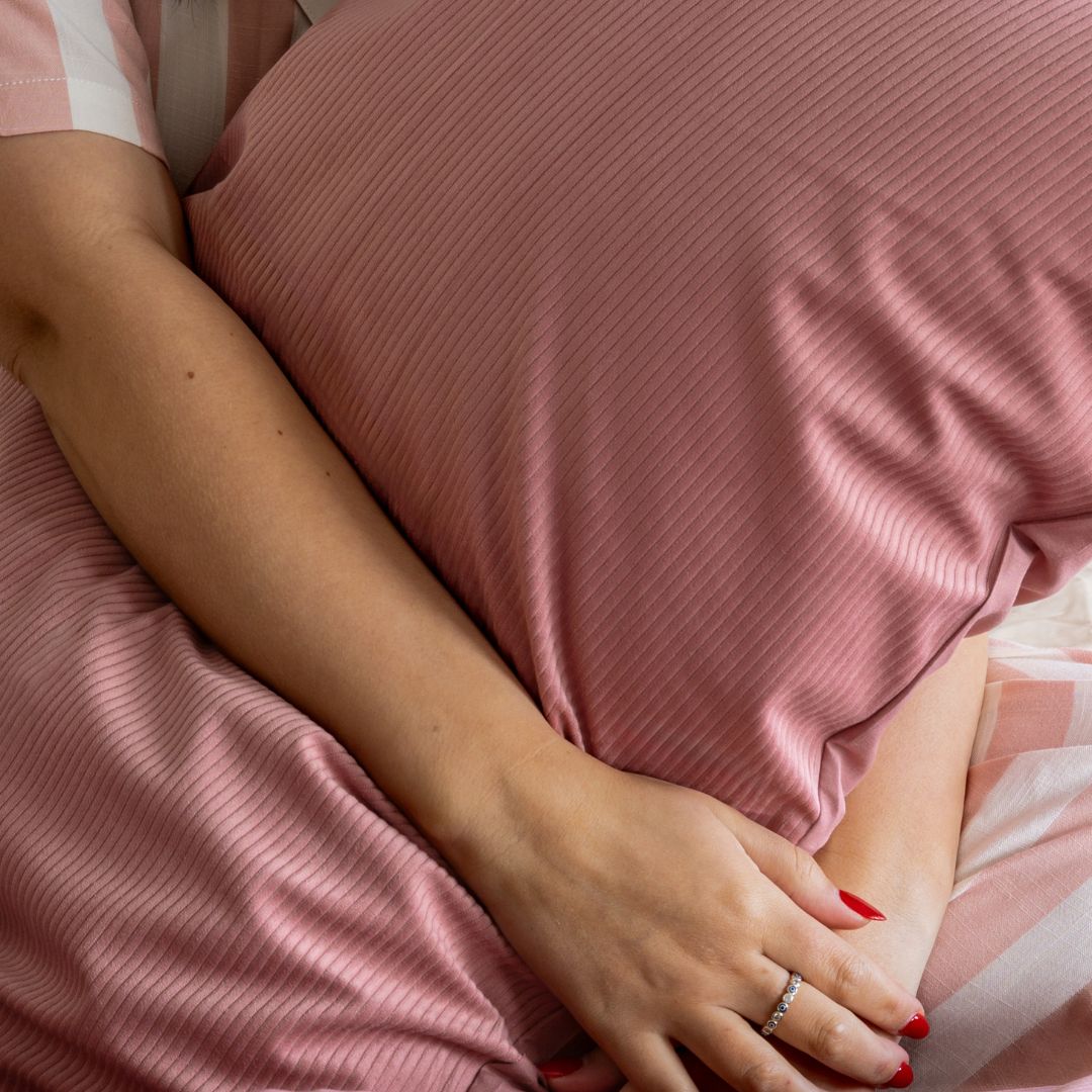 Close-up of a person's hands holding a pink pillow with a soft focus on the background.
