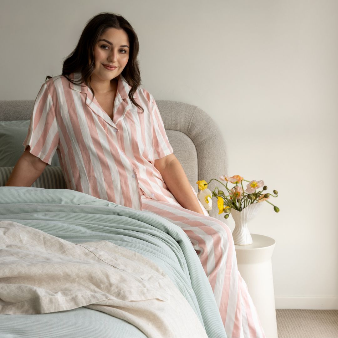 Woman in a striped nightshirt sitting on a bed with a vase of flowers in the background