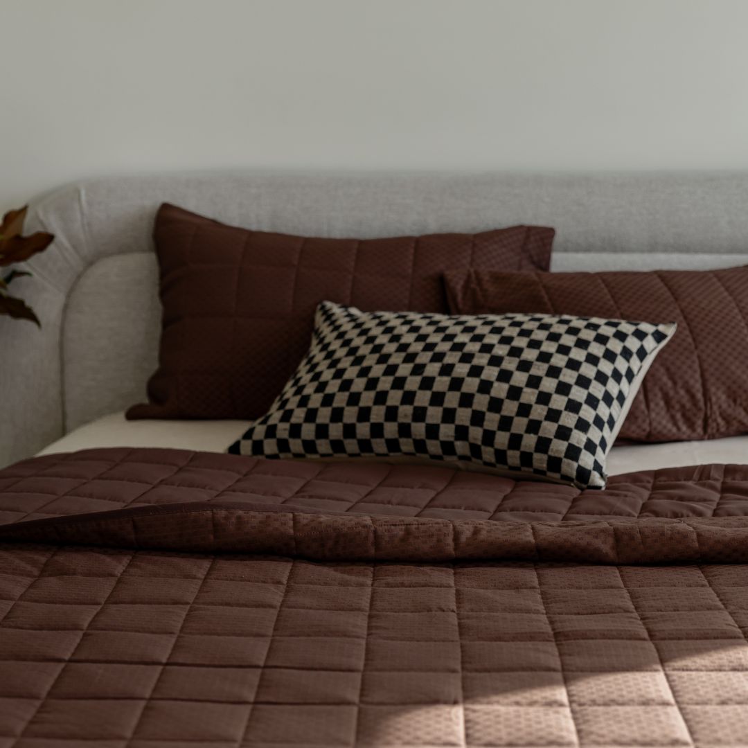 Brown quilt and pillows on a sofa against a neutral wall
