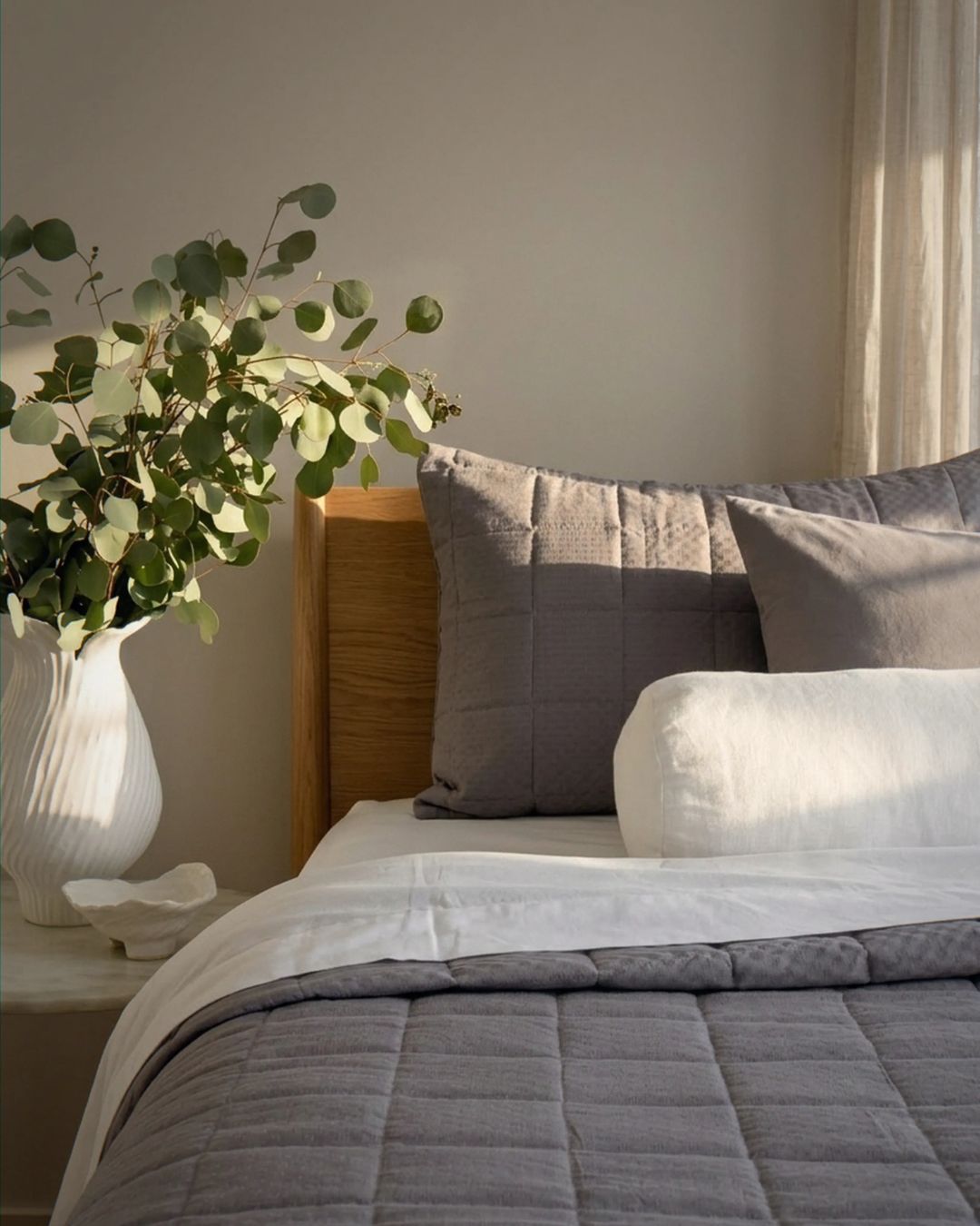 Bedroom with a bed featuring gray bedding and pillows, a vase with greenery on a nightstand.