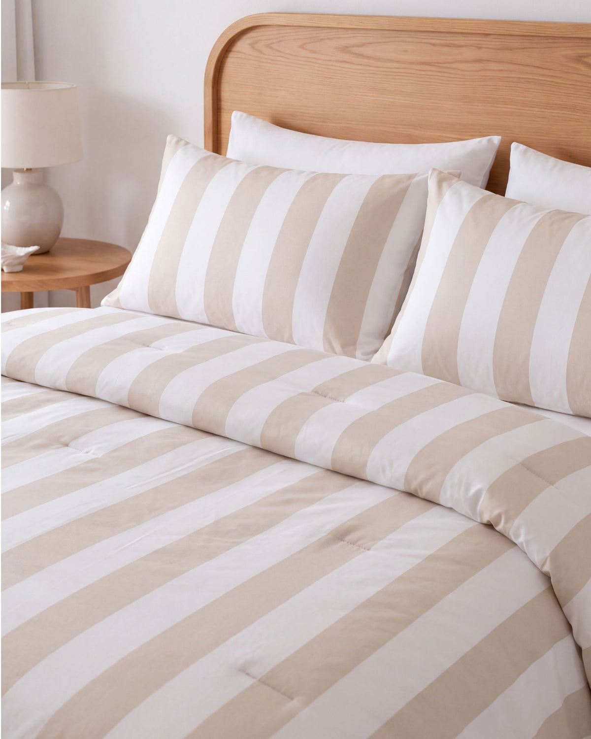 Striped bedding set with beige and white diagonal stripes on a bed with a wooden headboard, including two matching pillowcases and white pillows behind them.