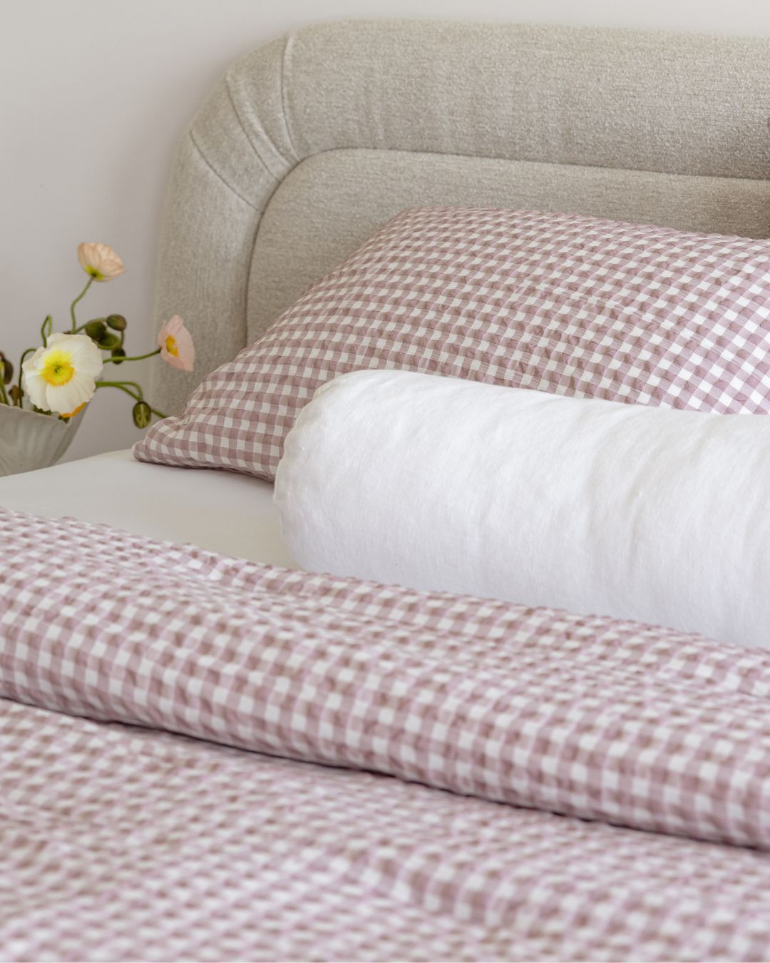 Bed with pink and white checkered bedding and pillows, featuring a neutral headboard.