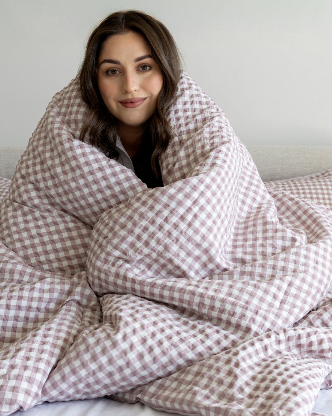 Woman wrapped in a pink and white checkered blanket against a plain background