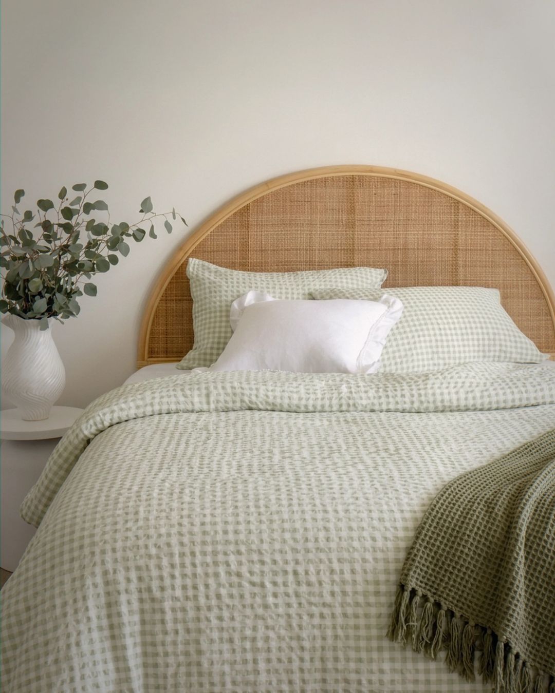 Bed with green checkered bedding and wicker headboard in a room setting.