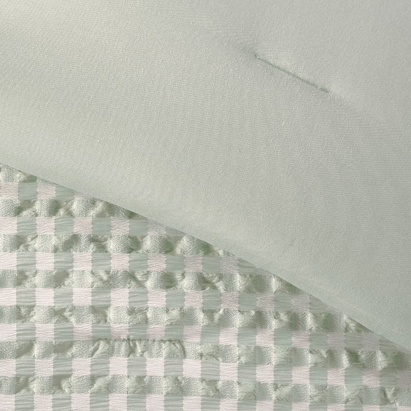 A calming bedroom displays the Morgan and Reid Eucalyptus Gingham Comforter Set on a neatly styled bed with matching pillowcases, rattan furniture, natural pendant lamp, indoor plant, and a woven rug.