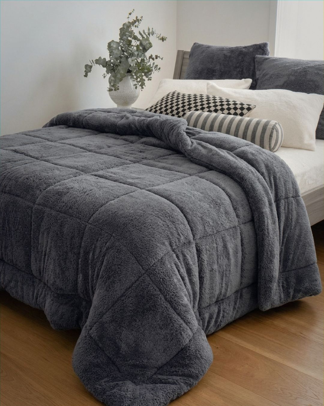 Gray comforter on a bed with pillows and a plant in the background