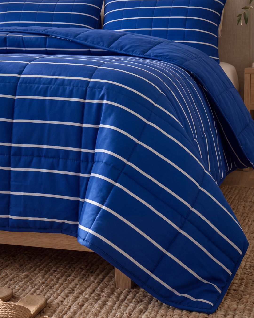 A blue quilted comforter with white horizontal stripes, styled on a bed with matching pillows in a bedroom setting.