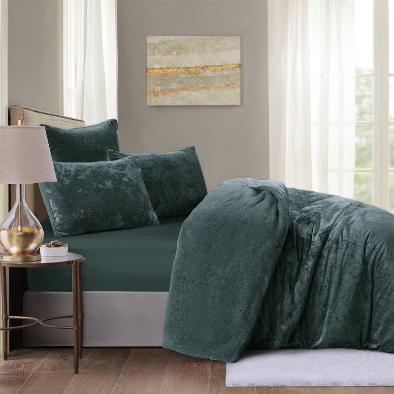Green velvet bedding set on a bed in a bedroom with a side table and lamp.
