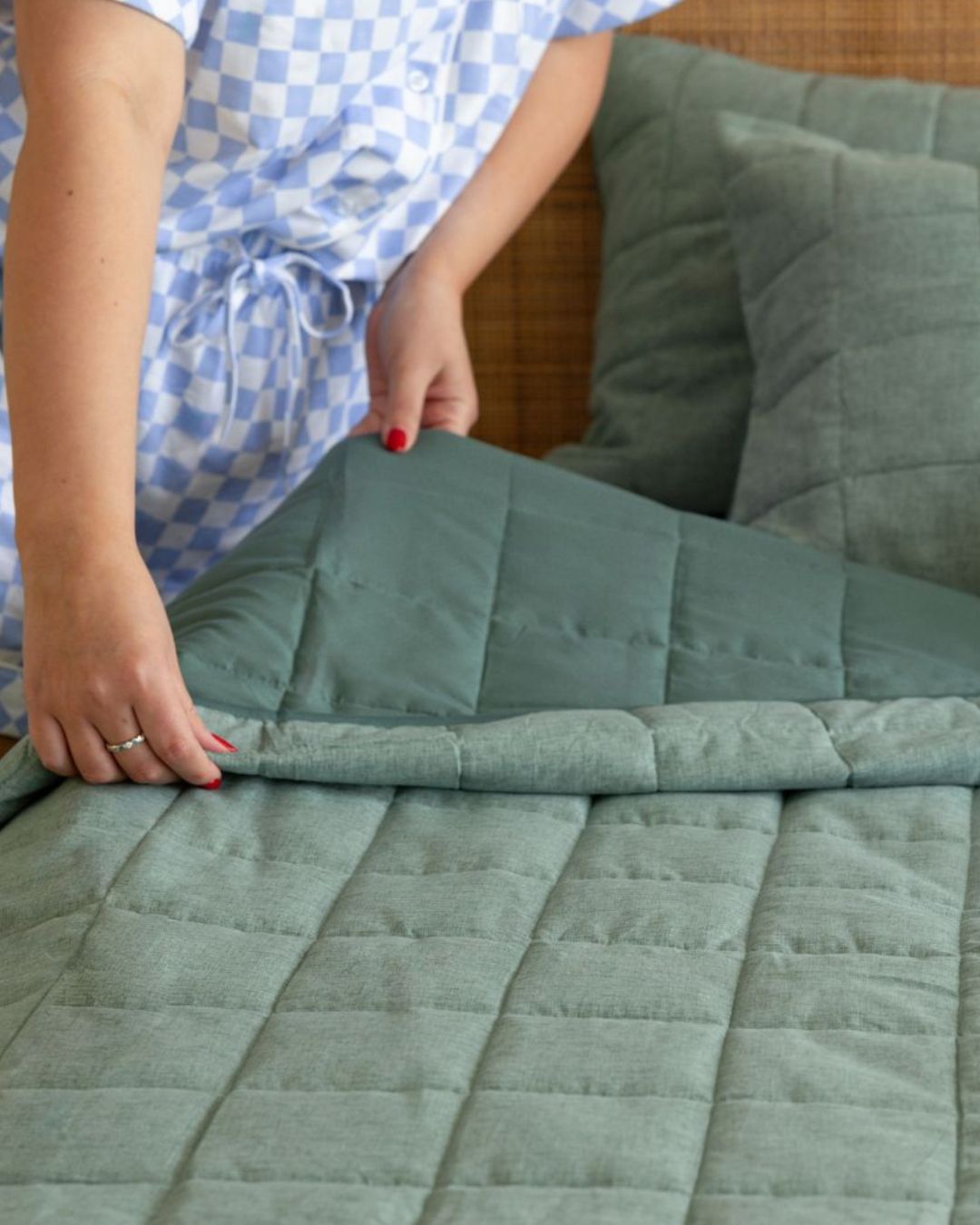 Person folding a green quilt on a couch