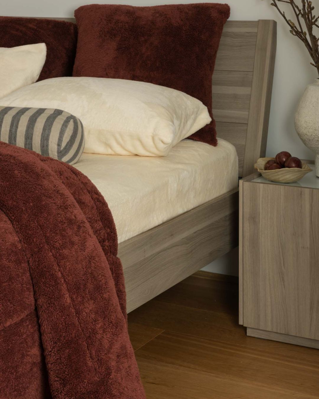 Bedroom scene with a bed featuring pillows and a blanket, next to a nightstand.