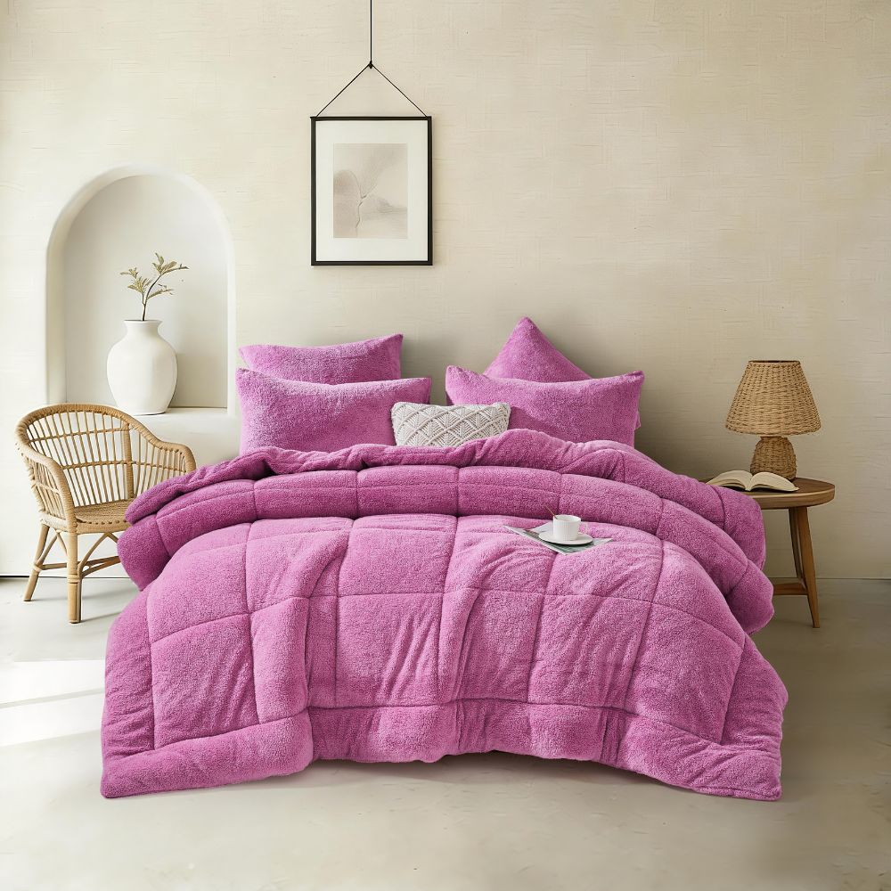 Purple comforter set on a bed in a bedroom with a chair and lamp in the background.