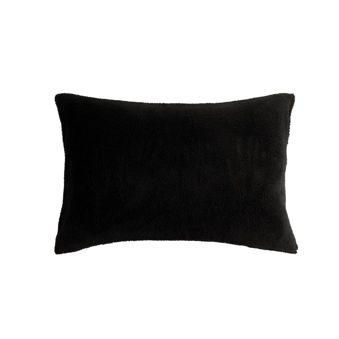 A modern bedroom features a neatly made bed with the Morgan and Reid Black Snuggle Fleece Comforter Set, accented by a white pillow, a side table with a plant and books, wall art, a pendant lamp, and sheer curtains letting in natural light.