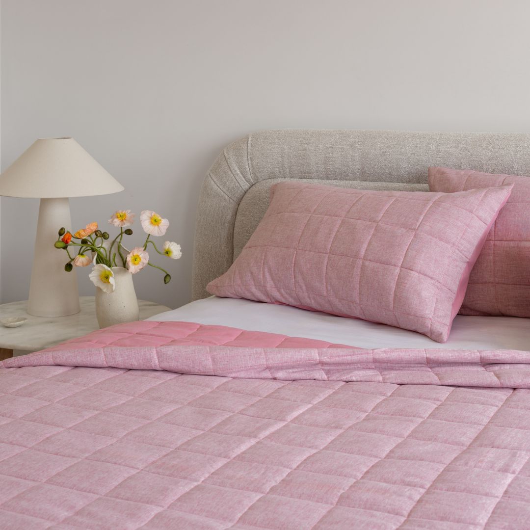 Bed with pink checkered bedding and pillows, nightstand with lamp and flowers.