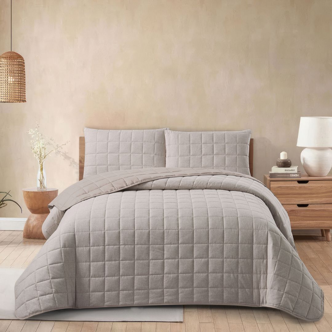 Gray quilt set on a bed in a bedroom with a beige wall and wooden nightstand.