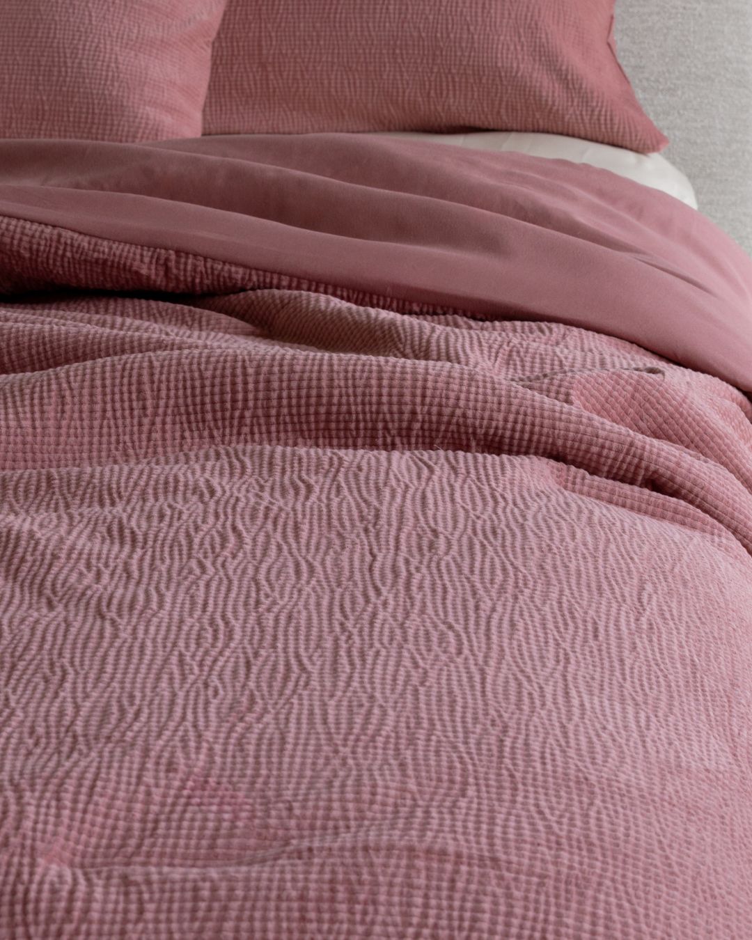 Close-up of textured pink bedding with a pillow in the background