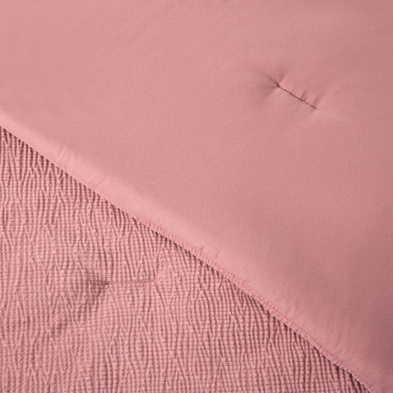 A modern bedroom features the Morgan and Reid Rose Stretch Woven Comforter Set on a neatly made bed with matching pillows, warm neutral walls, a woven pendant light, a wooden side table with a glass vase of white stems, and a ceramic lamp on a timber bedside table.