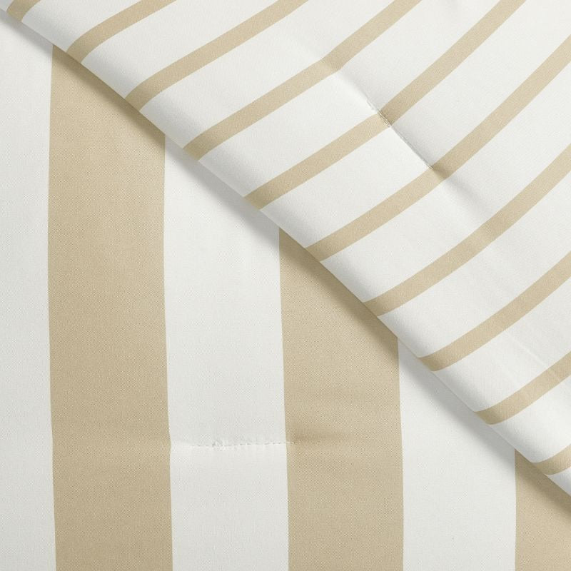 A coastal-inspired bedroom shows the Morgan and Reid Driftwood Stripe Comforter Set on a neatly made bed with striped pillowcases, rattan headboard, soft neutral walls, woven pendant light, and a round wooden side table.