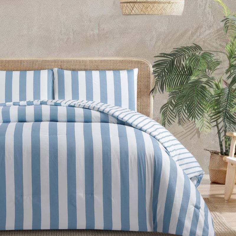 A fresh coastal bedroom features the Morgan and Reid Sea Breeze Stripe Comforter Set on a neatly styled bed with striped pillows, rattan bedhead, textured rug, natural pendant lighting, and a leafy plant beside the bed.