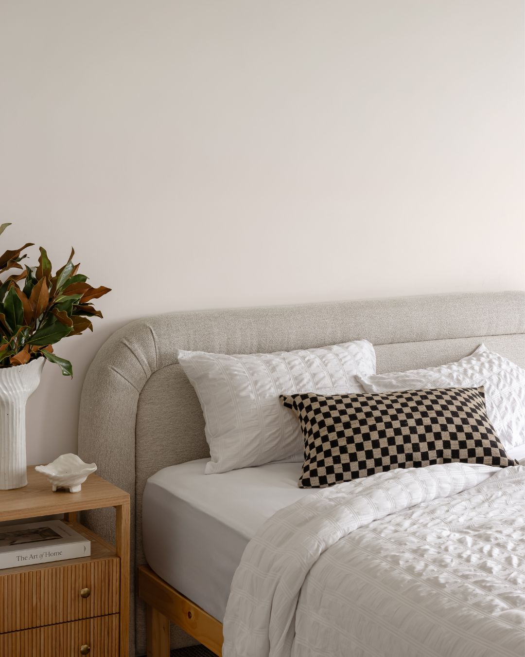 Neatly made bed with checkered pillow and plant on bedside table in a bedroom.
