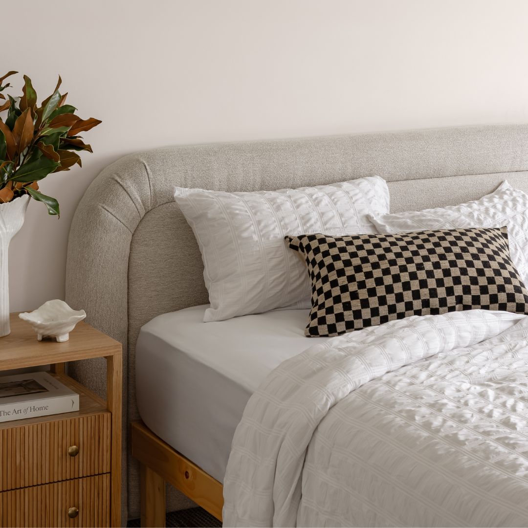 Neatly made bed with checkered pillow and nightstand with decor items