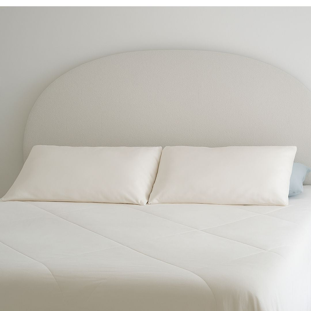 A neatly made bed with white pillows and Sienna Living Cooling 2 in 1 Pillowcase Pair sits beside a white nightstand with a black tissue box and beige bowl, all set against a minimal white wall for a refreshing sleep surface.