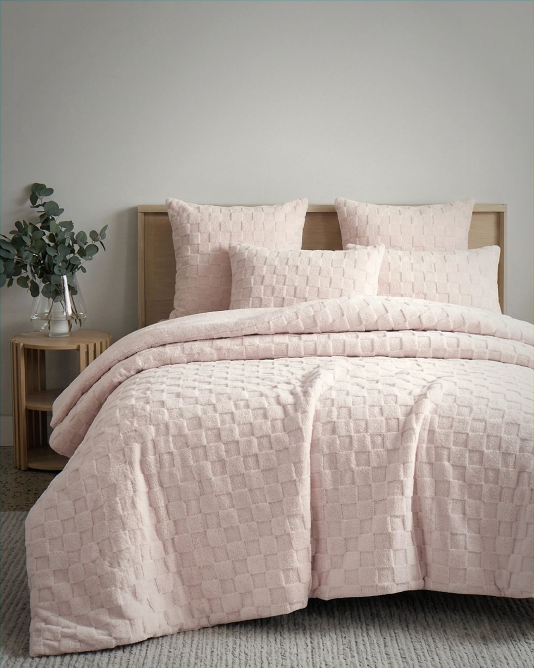 Soft pink checkered snuggle fleece comforter set styled on bed with matching pillow shams and wooden headboard