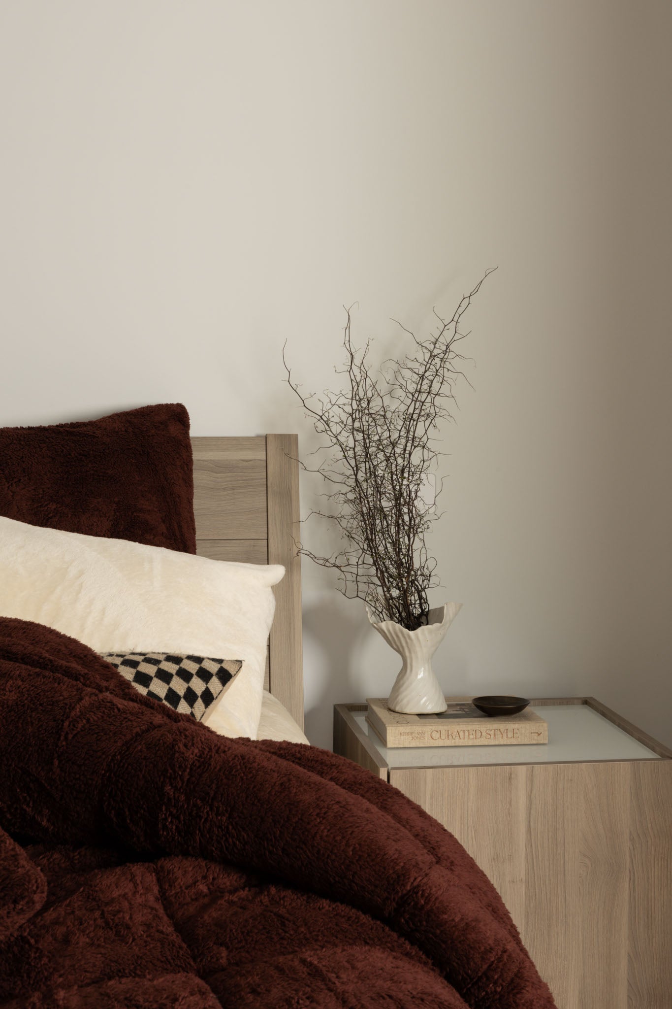 Bedroom with brown bedding, white pillows, and a vase with branches on a nightstand.