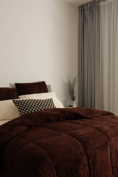 Brown comforter on a bed with pillows in a bedroom setting.