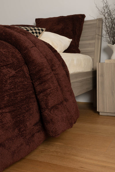 Brown textured blanket draped over a bed with pillows in a bedroom setting.