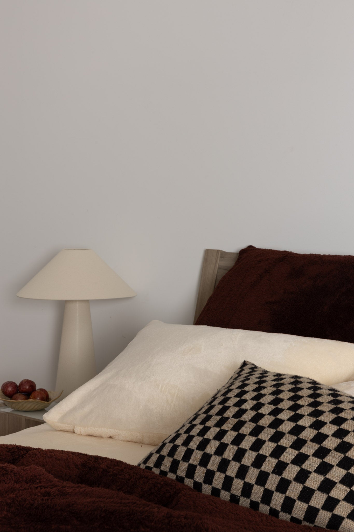 Bedroom with a bed featuring a checkered blanket, brown pillows, and a nightstand with a lamp.
