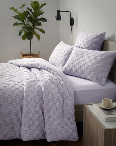 Lavender checkered snuggle fleece comforter set styled on bed with matching pillows and fiddle leaf fig plant