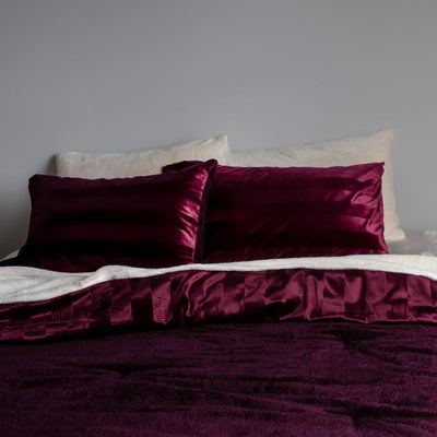 Red satin pillows on a bed against a gray wall