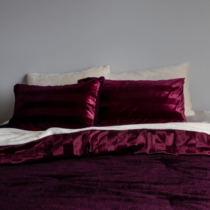 Red satin pillows on a bed against a gray wall