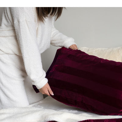 Person wearing a white robe holding a burgundy blanket over a bed.