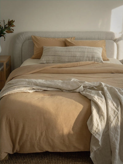 Neatly made bed with beige bedding and pillows in a softly lit bedroom.