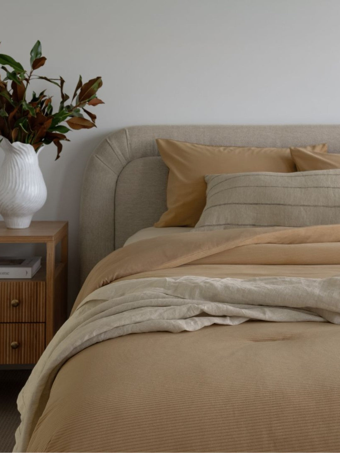 Neatly made bed with beige bedding in a bedroom setting.