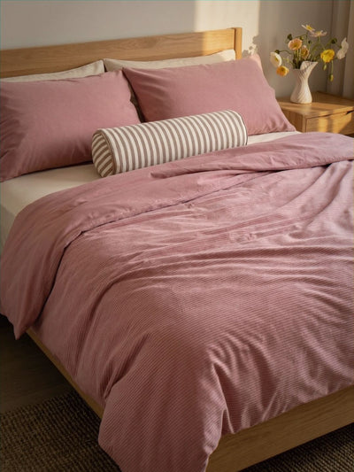 Pink bedding set on a bed with a wooden headboard and striped pillow.