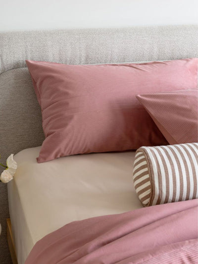Pink striped pillows and duvet on a bed with a neutral headboard.