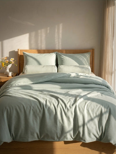 Bed with light green bedding and pillows in a softly lit room.
