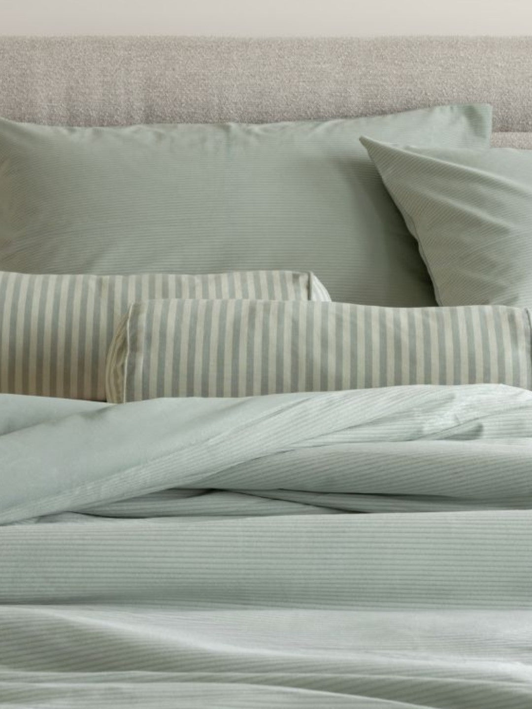 Light green bedding set with striped pillows on a bed.