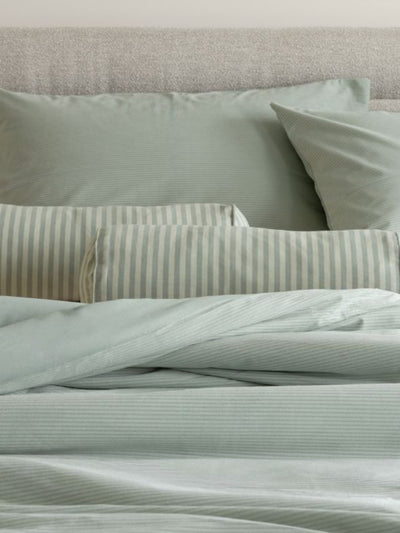 Light green bedding set with striped pillows on a bed.