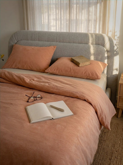 Bed with pink bedding and pillows, open book, and glasses in a softly lit room.
