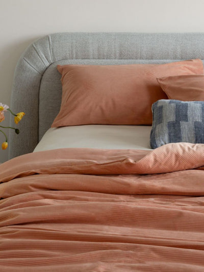 Bed with pink bedding and pillows against a gray headboard