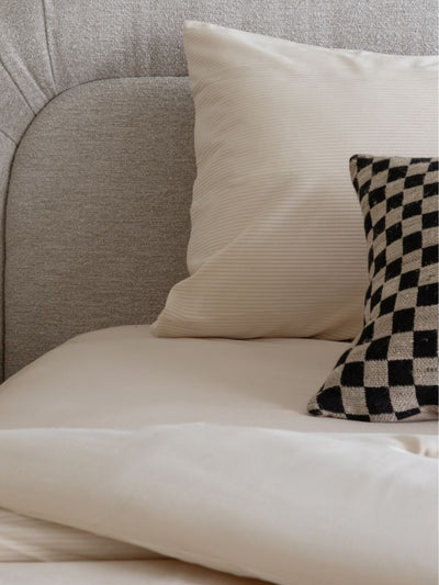 Beige sofa with a white pillow and a black and white checkered pillow.